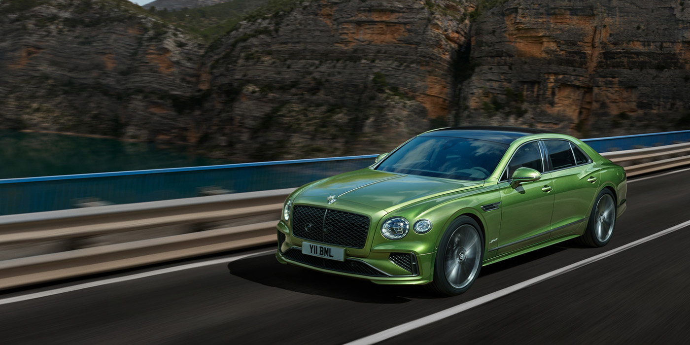 Bentley Vilnius Bentley New Flying Spur Speed v8 hybrid sedan driving dynamically on a mountain road in Tourmaline Green paint