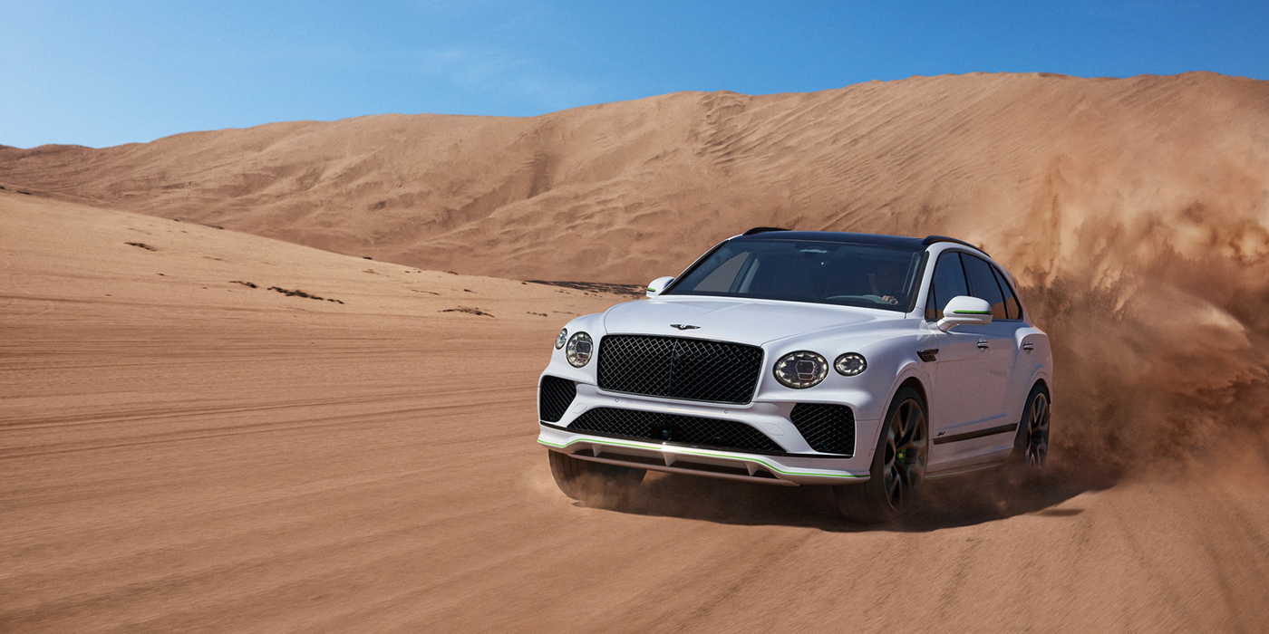 Bentley Vilnius Bentley Bentayga Speed SUV front three quarter in Snow Quarts Pearlescent by Mulliner white paint driving dynamically through the desert