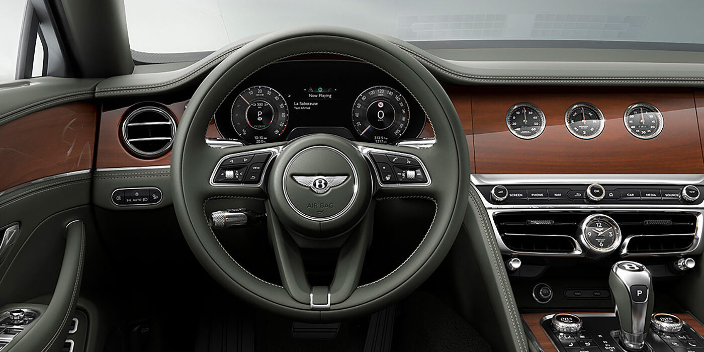 Bentley Vilnius New Bentley Flying Spur sedan front cabin in Cumbrian Green hide and Crown Cut walnut veneer showing steering wheel and Rotating Display with three clocks on face