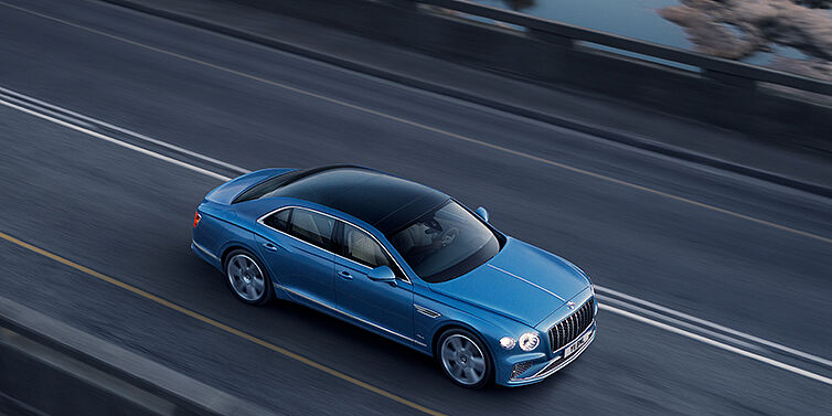 Bentley Vilnius New Bentley Flying Spur Azure sedan in Light windsor blue paint by Mulliner, with 22 inch Azure wheels seen from overhead driving dynamically on a country road