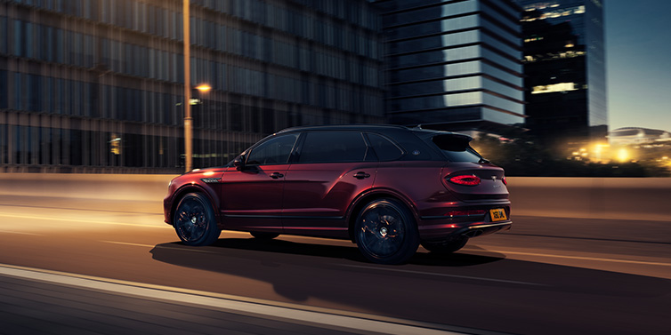 Bentley Vilnius Bentley Bentayga Extended Wheelbase Mulliner SUV in Cricket Ball red paint driving dynamically in city at night